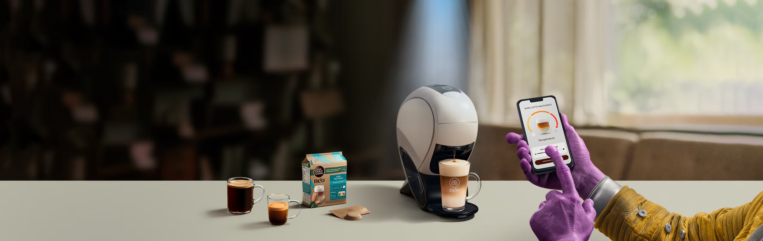 Une main d'Alien utilisant l’application NESCAFÉ Dolce Gusto pour personnaliser un café. Machine à latte intelligente NEO, pack de café et boissons.