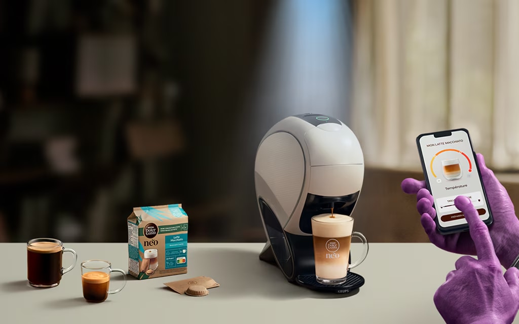 Une main d'Alien utilisant l’application NESCAFÉ Dolce Gusto pour personnaliser un café. Machine à latte intelligente NEO, pack de café et boissons.