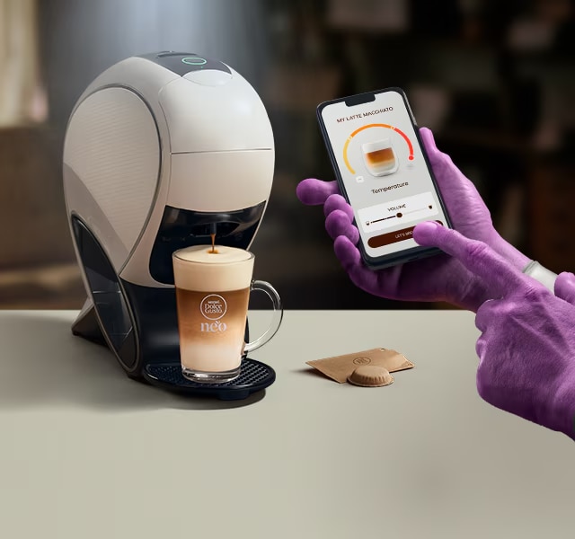 Une main d'Alien utilisant l’application NESCAFÉ Dolce Gusto pour personnaliser un café. Machine à latte intelligente NEO, pack de café et boissons.