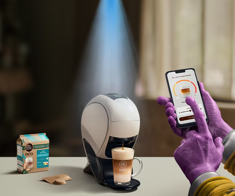 Une main d'Alien utilisant l’application NESCAFÉ Dolce Gusto pour personnaliser un café. Machine à latte intelligente NEO, pack de café et boissons.