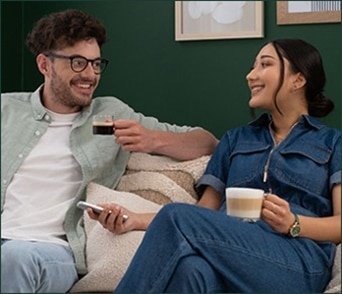 Un couple souriant se détend sur un canapé, dégustant ensemble un café NESCAFÉ Dolce Gusto.